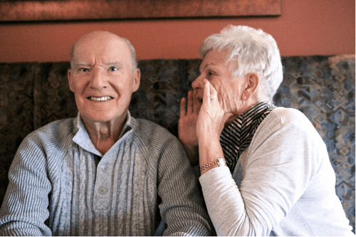 Older woman whispering into the ear of an elderly man