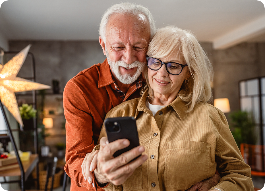 Smiling senior couple using smartphone together, representing easy app-based control of Audien hearing aids

