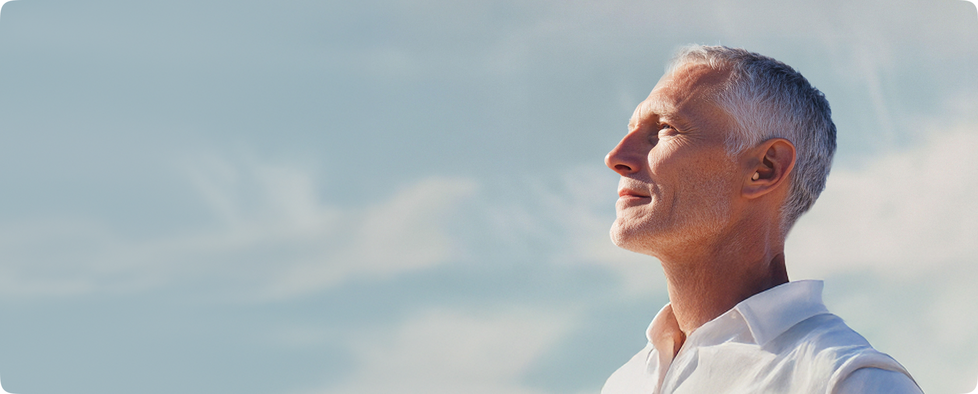 Man with gray hair looking upwards wearing a hearing aid 