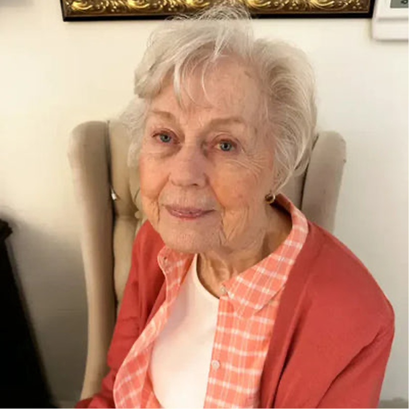 Elderly woman smiling while seated, sharing positive experience as Audien hearing aid user

